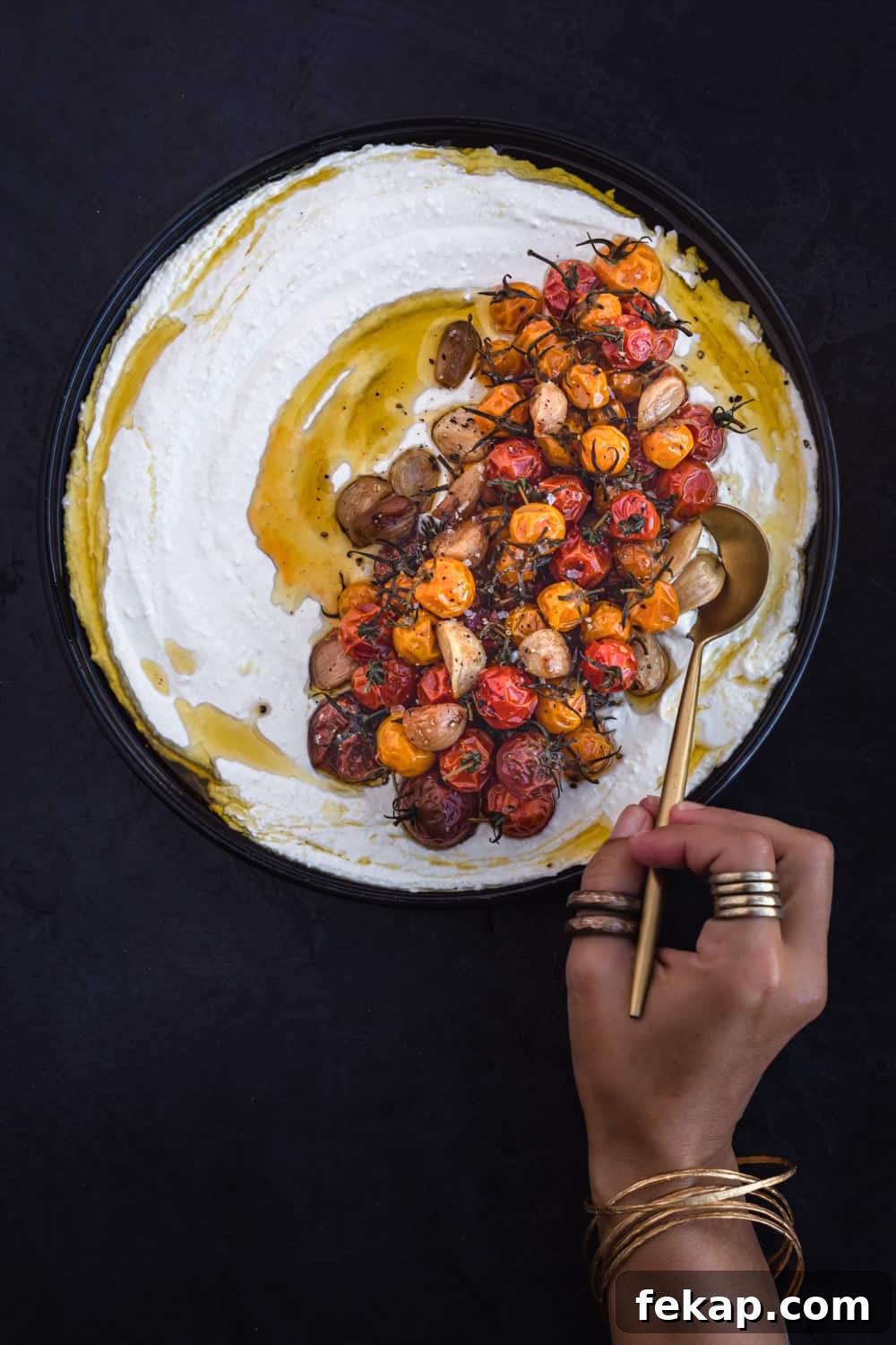 Daniela Gerson dipping a gold spoon into a plate of tomato confit with whipped yogurt; overhead shot.