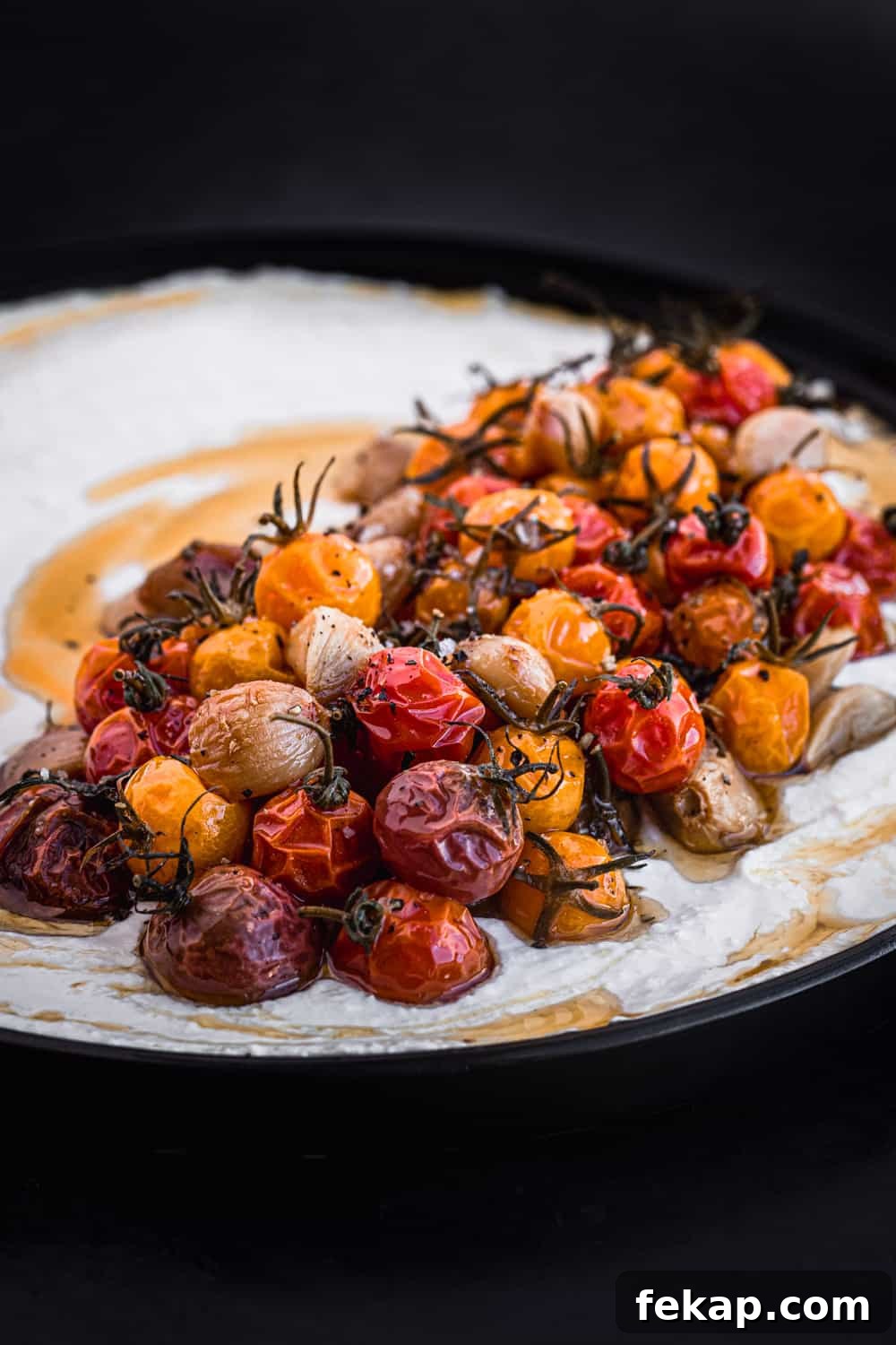 Cherry tomato confit on whipped yogurt; side angle shot on a black plate.