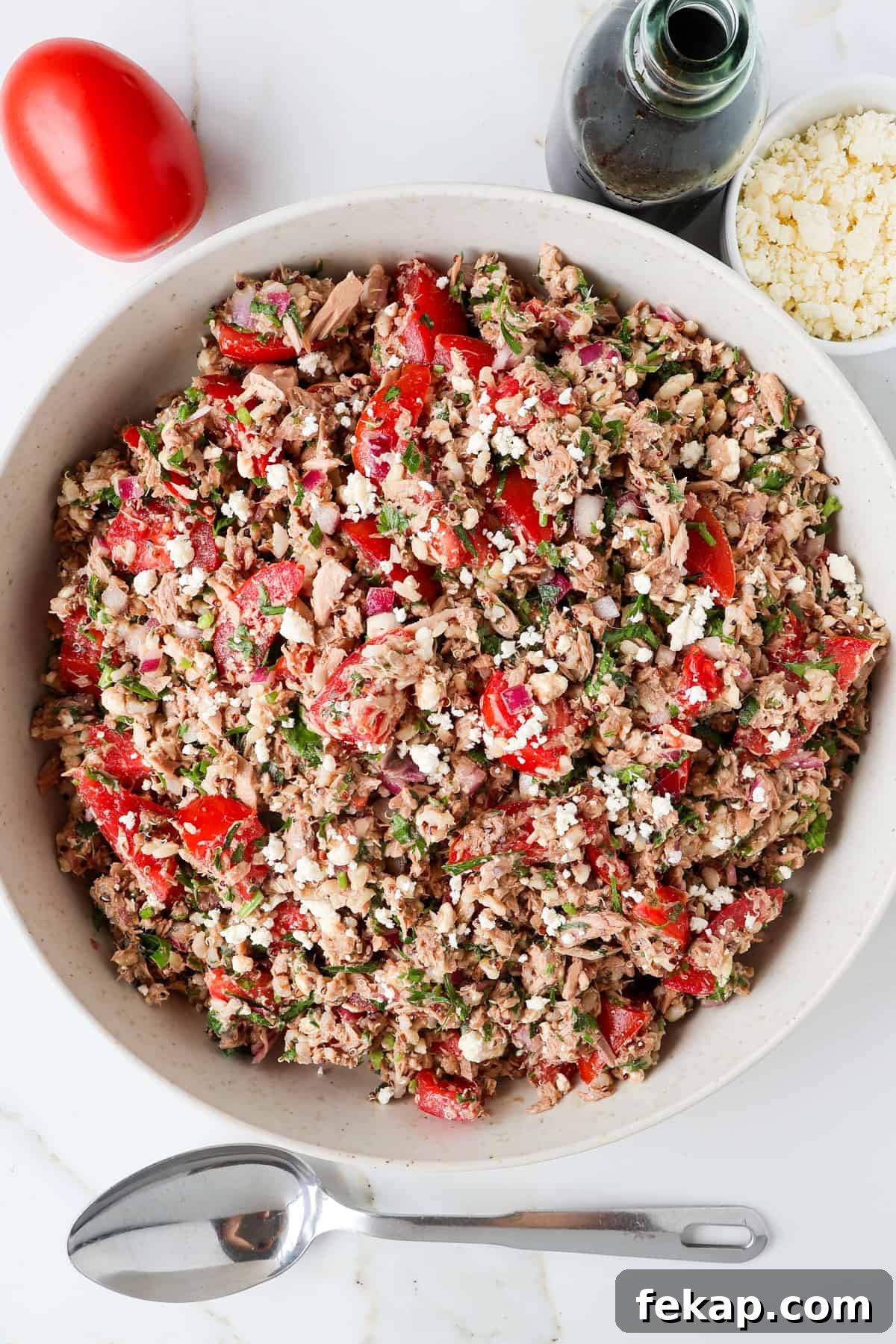 Mediterranean Tuna and Tomato Salad Recipe 2 Tuna tomato salad with balsamic vinegar in a bottle, feta cheese, a tomato and spoon on the sides.