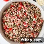Tuna tomato salad with balsamic vinegar in a bottle, feta cheese, a tomato and spoon on the sides.
