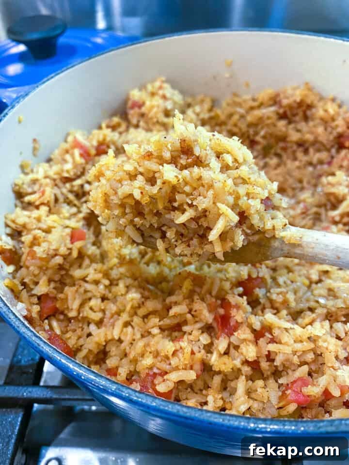 Restaurant-Style Mexican Fried Rice Recipe 15 A pot full of cooked Mexican rice with a wooden spoon scooping out a serving.