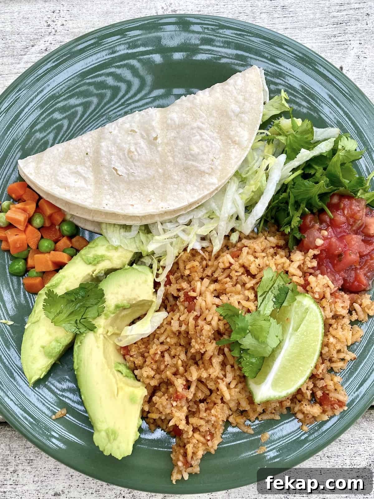 Restaurant-Style Mexican Fried Rice Recipe 4 A plate with a serving of Mexican rice, topped with lime and avocado, peas and carrots and salsa on the side.