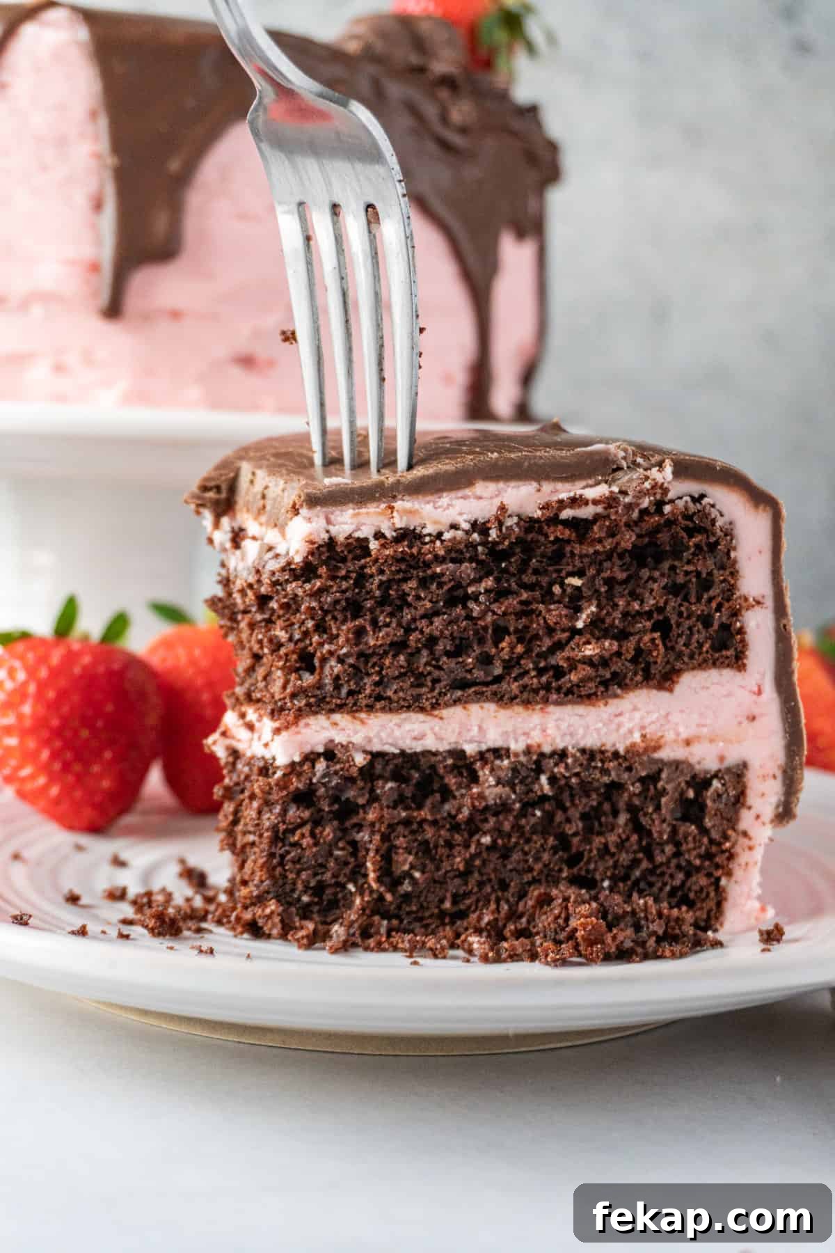 Moist Chocolate Strawberry Cake Recipe 2 sticking a fork into a slice chocolate cake with pink frosting.