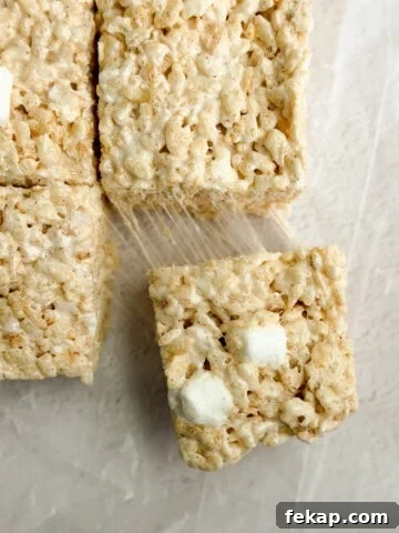 Fudgy Double Chocolate Cookie Bars Recipe 12 a close up of brown butter rice krispie treats with a marshmallow being pulled and stretched.