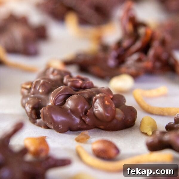 A peanut cluster dipped in chocolate sits on parchment paper.