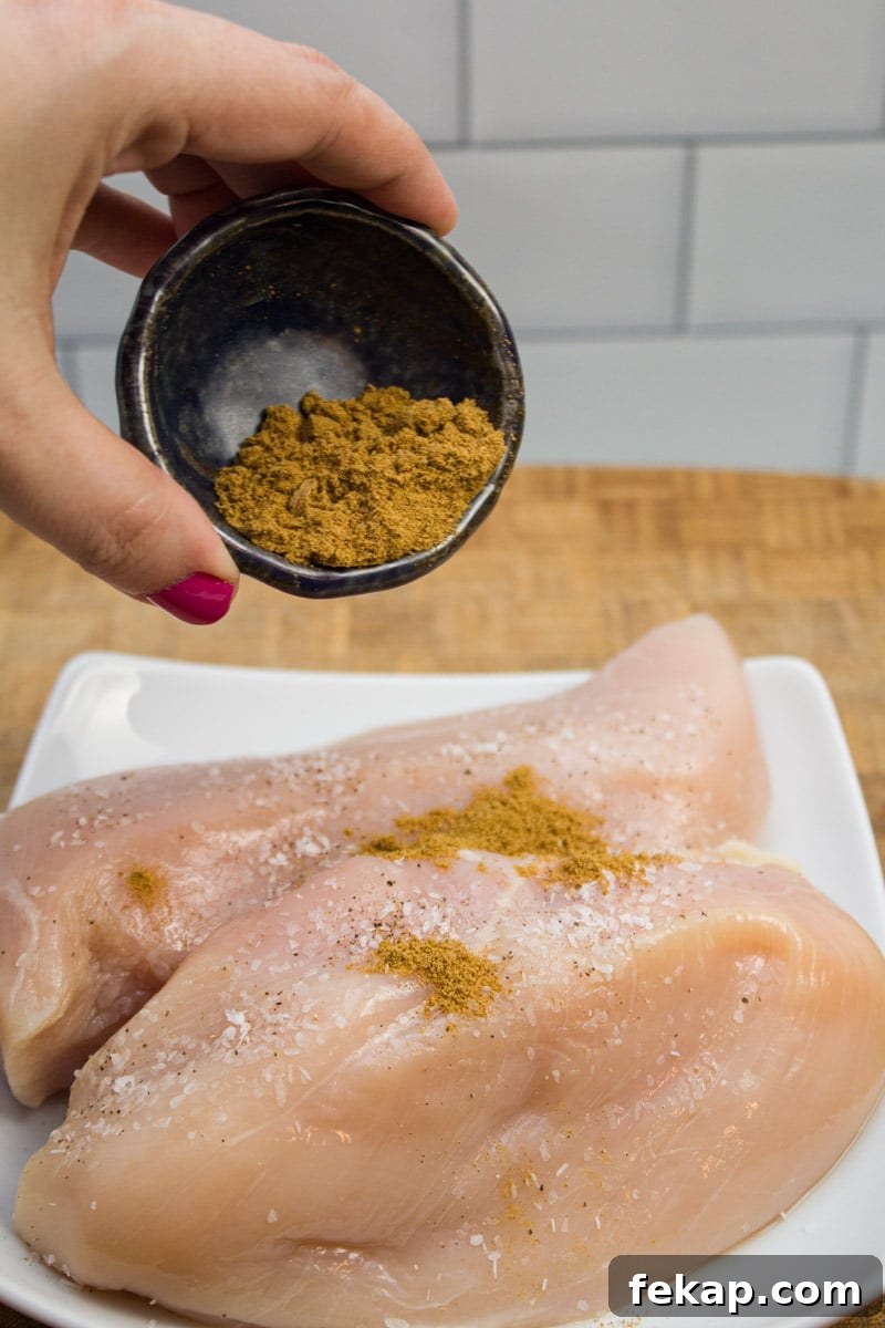 Seasoning chicken breasts with ground cumin.