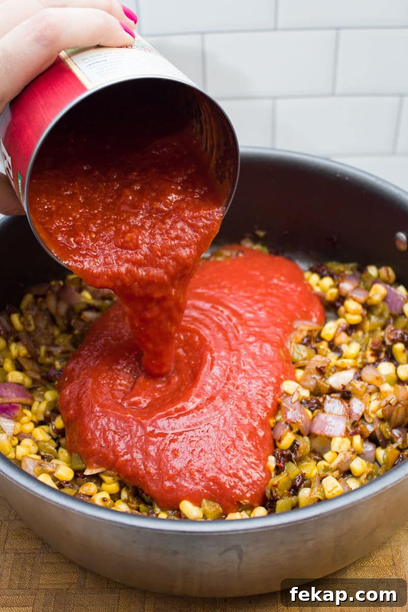 Adding canned tomatoes to a sauté pan full of veggies.
