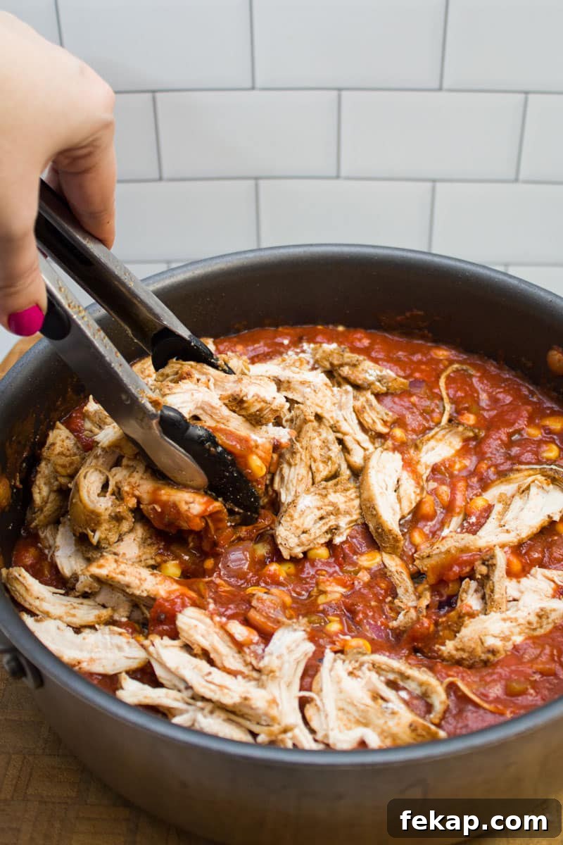 Mixing together chicken enchilada filling in a sauté pan.