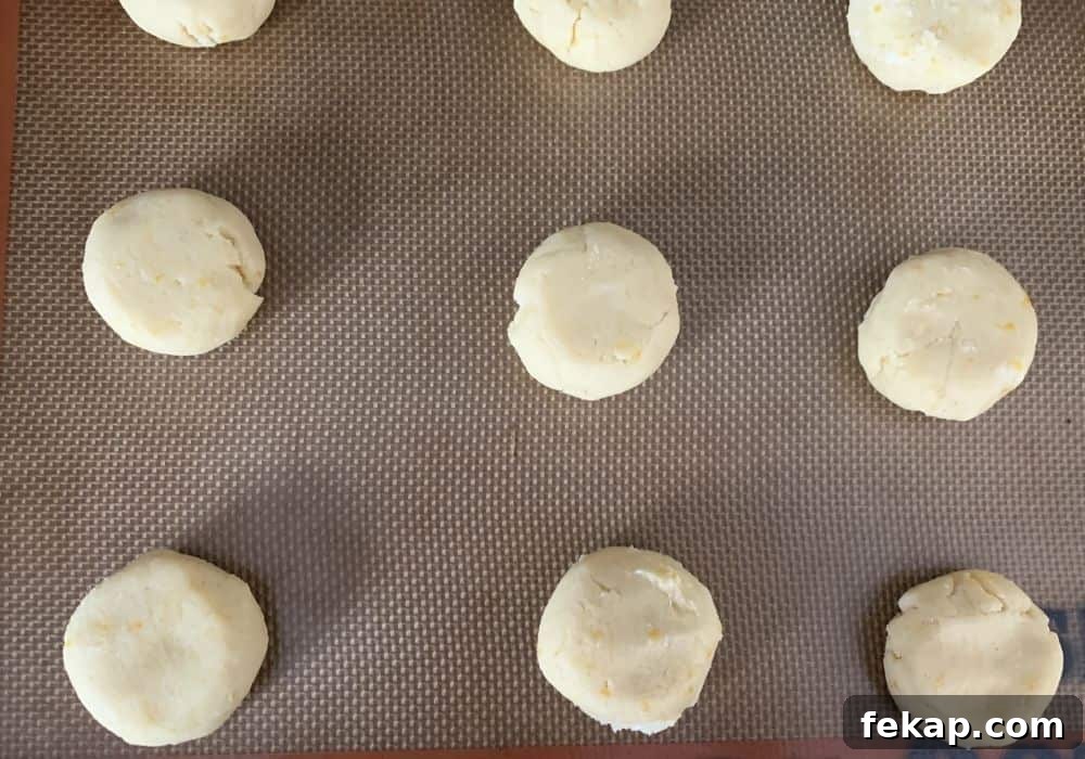 several rounds of slightly flattened lemon cookie dough on a lined baking sheet, ready to be baked