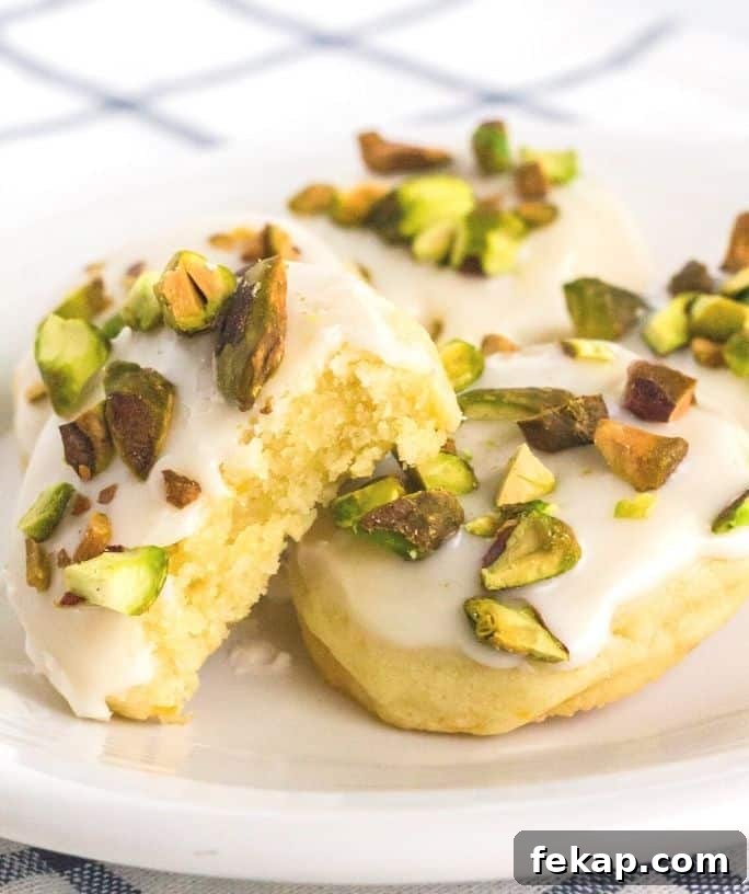 a few lemon pistachio cookies on a white plate, with a bite taken out of one.