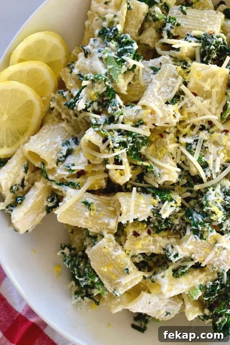 Lemon ricotta pasta with kale in a white bowl with lemon slices next to it.