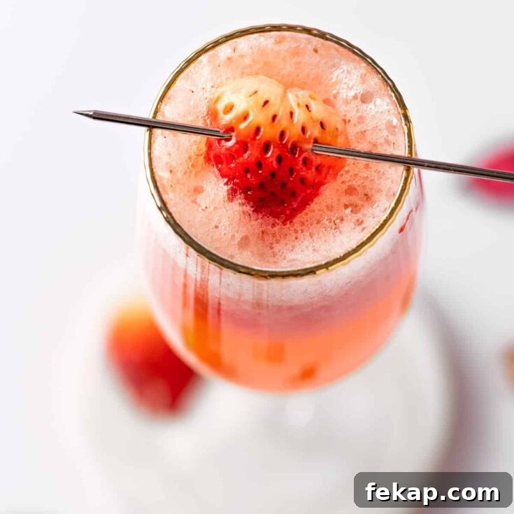A strawberry bellini with Prosecco, garnished with a strawberry slice, on a white table.