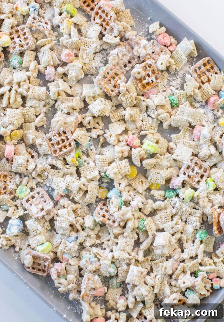 Lucky Charms Puppy Chow: Leprechaun Bait Recipe 5 A baking sheet filled with a colorful snack mix of pretzels, Chex cereal, mini marshmallows, coated in a white powdered coating, likely powdered sugar.