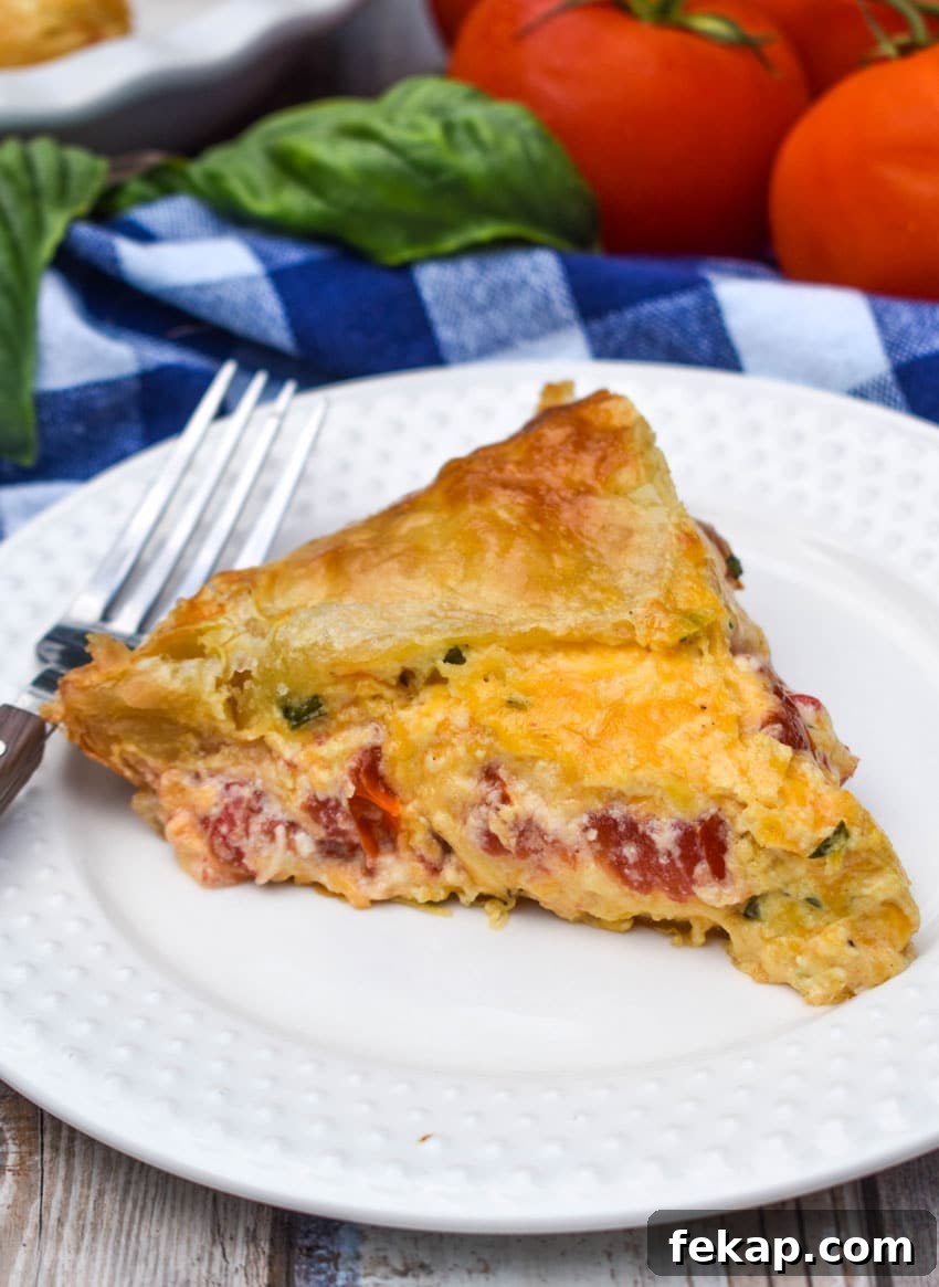 Savory Tomato Pie with Flaky Puff Pastry Crust 2 a slice of tomato pie with puff pastry crust on a small white plate with a fork resting on the side