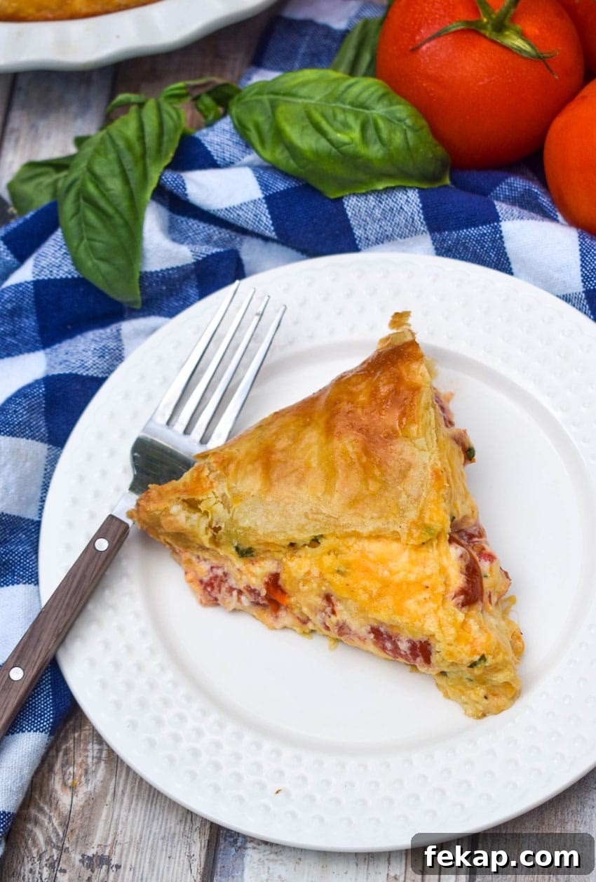 Savory Tomato Pie with Flaky Puff Pastry Crust 6 a slice of tomato pie with puff pastry crust on a small white plate with a fork resting on the side