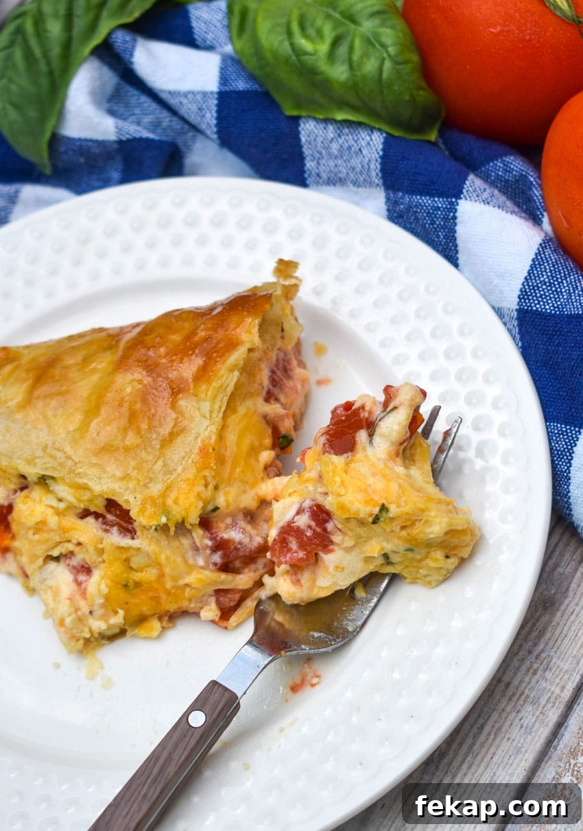 Savory Tomato Pie with Flaky Puff Pastry Crust 7 a slice of tomato pie with puff pastry crust on a small white plate with a fork resting on the side