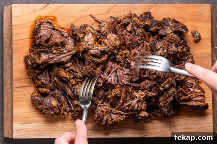 Korean BBQ Shredded Beef Burritos Recipe 5 shredding cooked beef on a cutting board with two forks