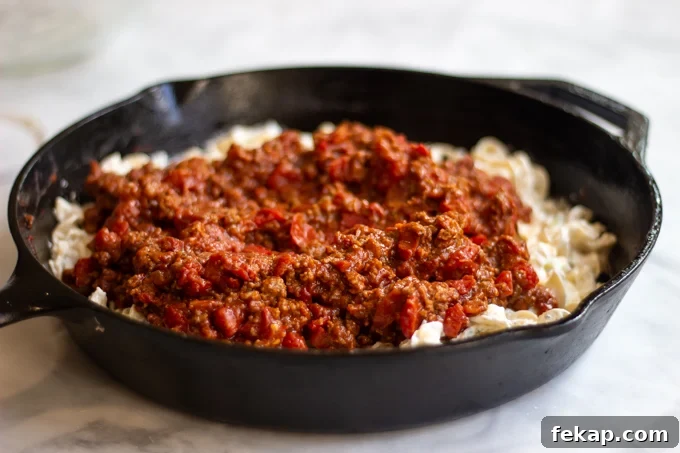 A skillet of egg noodles mixture topped with ground beef and tomato sauce