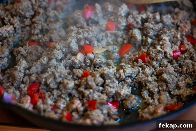 Ground beef browning in a skillet with onions and red bell peppers