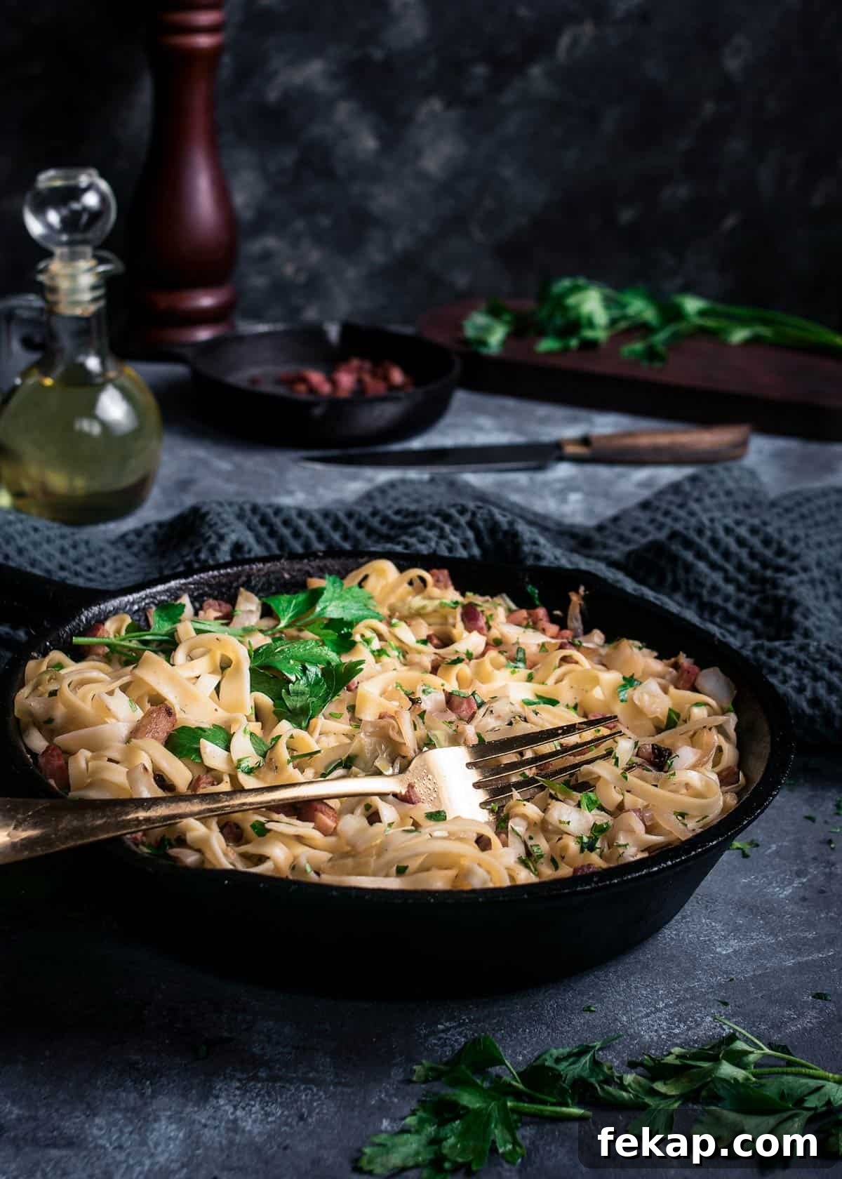 Classic Haluski: Fried Cabbage and Noodles with Bacon 9 A skillet with haluski sprinkled with fresh parsley on a table with fork.