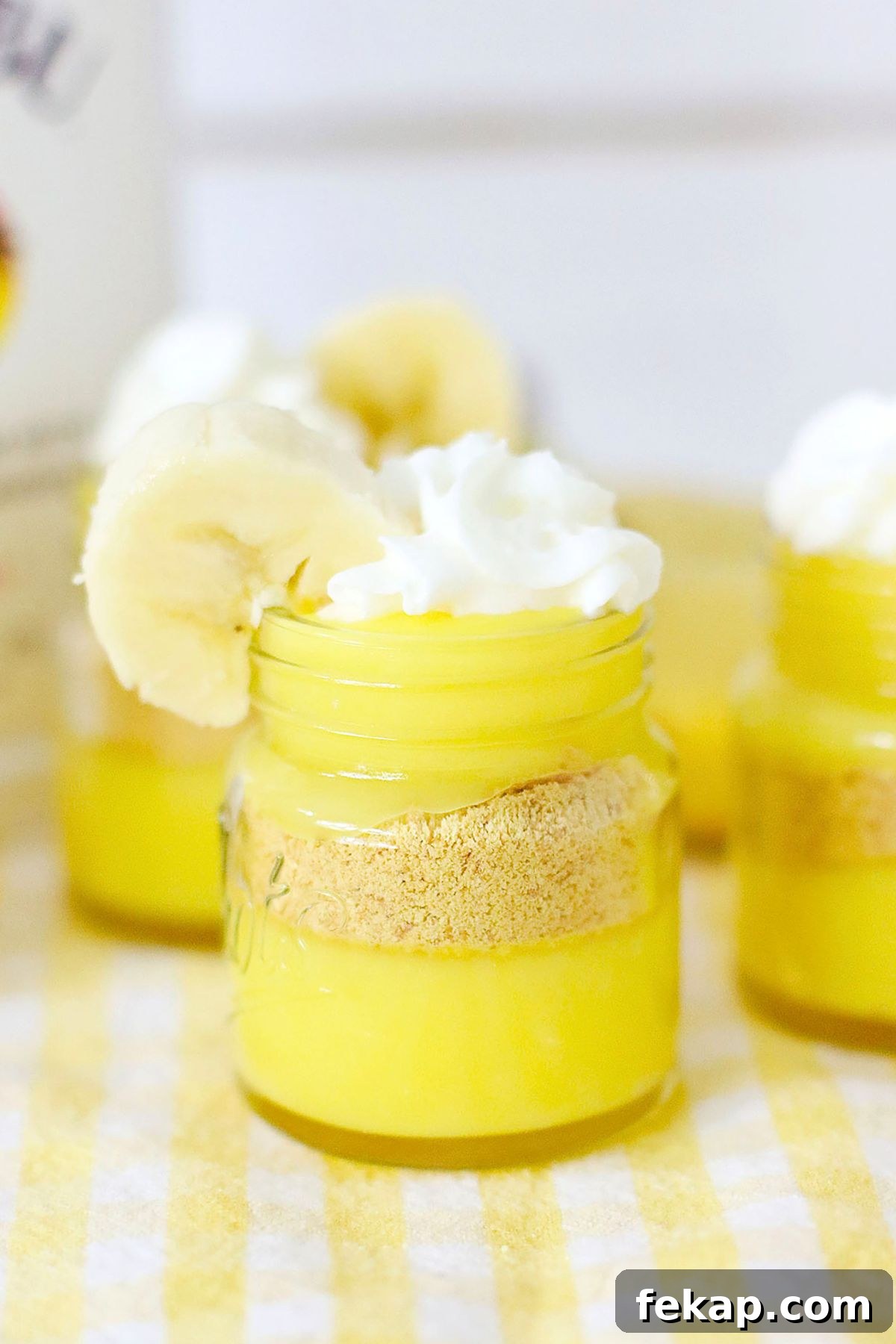 Creamy Banana Pudding Shots Recipe for Parties 2 Bright yellow pudding layers in mini jars, topped with whipped cream and garnished with a banana slice.