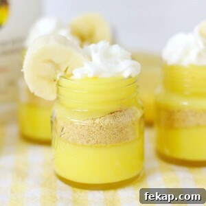 Bright yellow pudding layers in mini jars, topped with whipped cream and garnished with a banana slice.