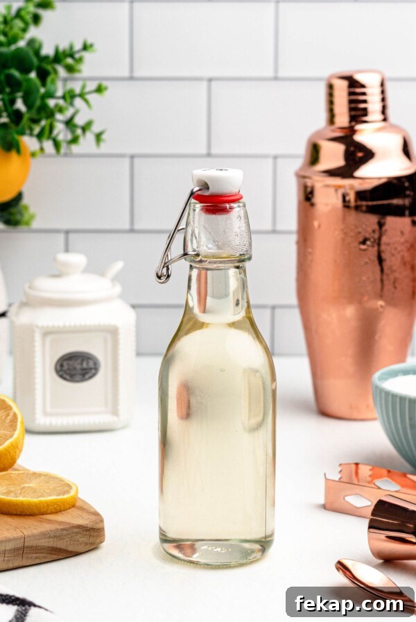 Clear glass bottle of simple syrup on a table, with lemon slices and bar mixing tools next to the bottle.