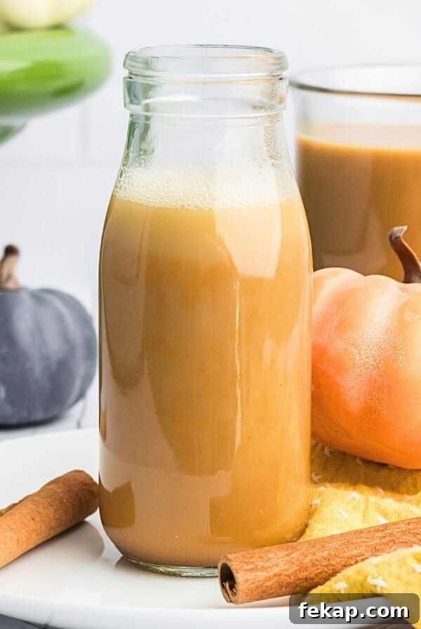 Creamy pumpkin spice creamer in a clear glass bottle with small pumpkins around it.