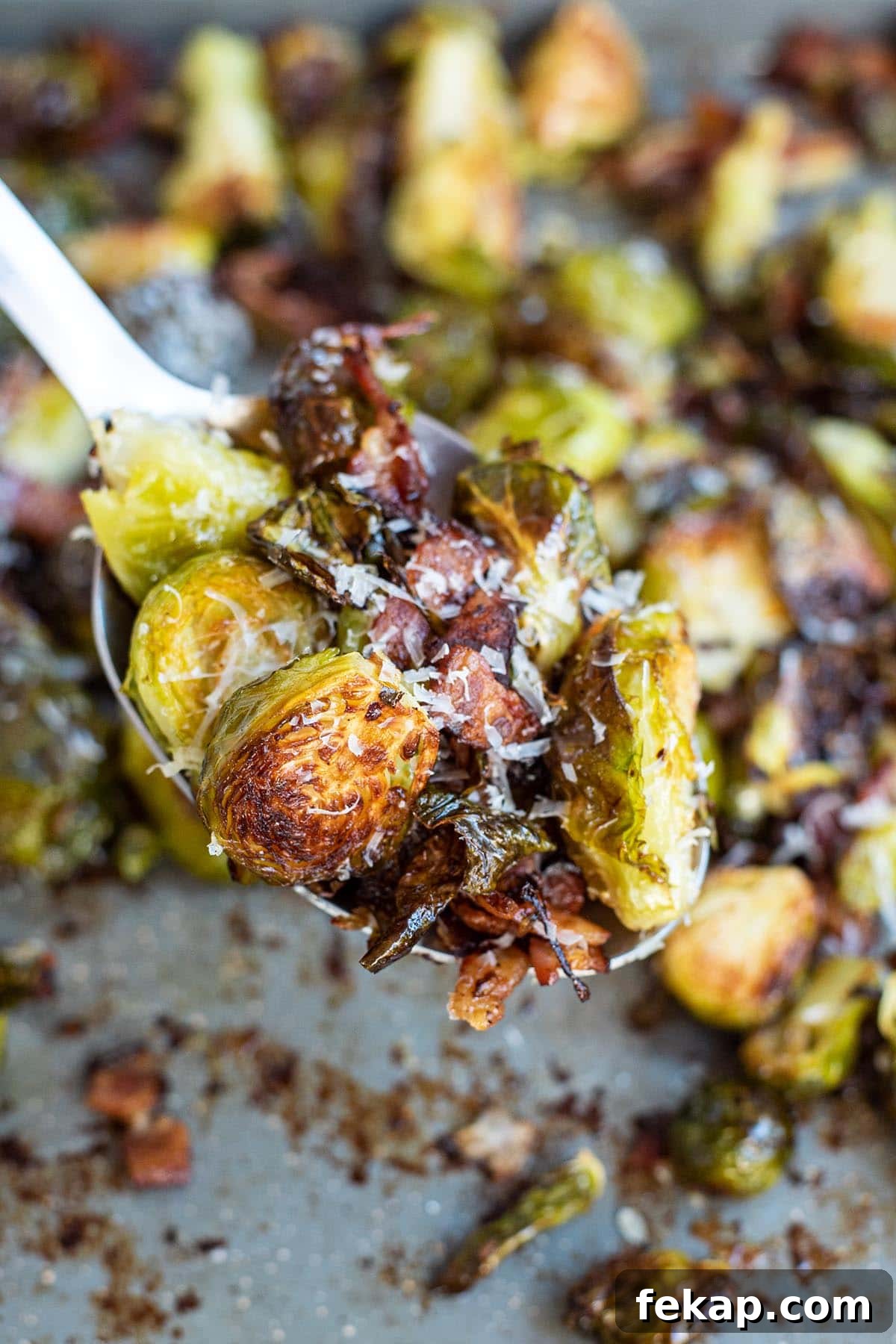 A close up of a spoon holding golden crispy roasted Brussels sprouts with bacon and parmesan cheese.
