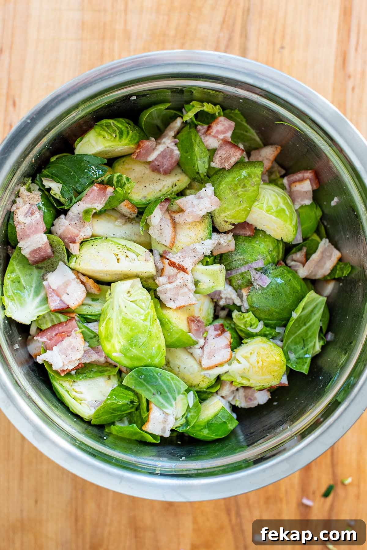 Uncooked Brussels sprouts, chopped shallots, and chopped bacon in a stainless steel bowl.