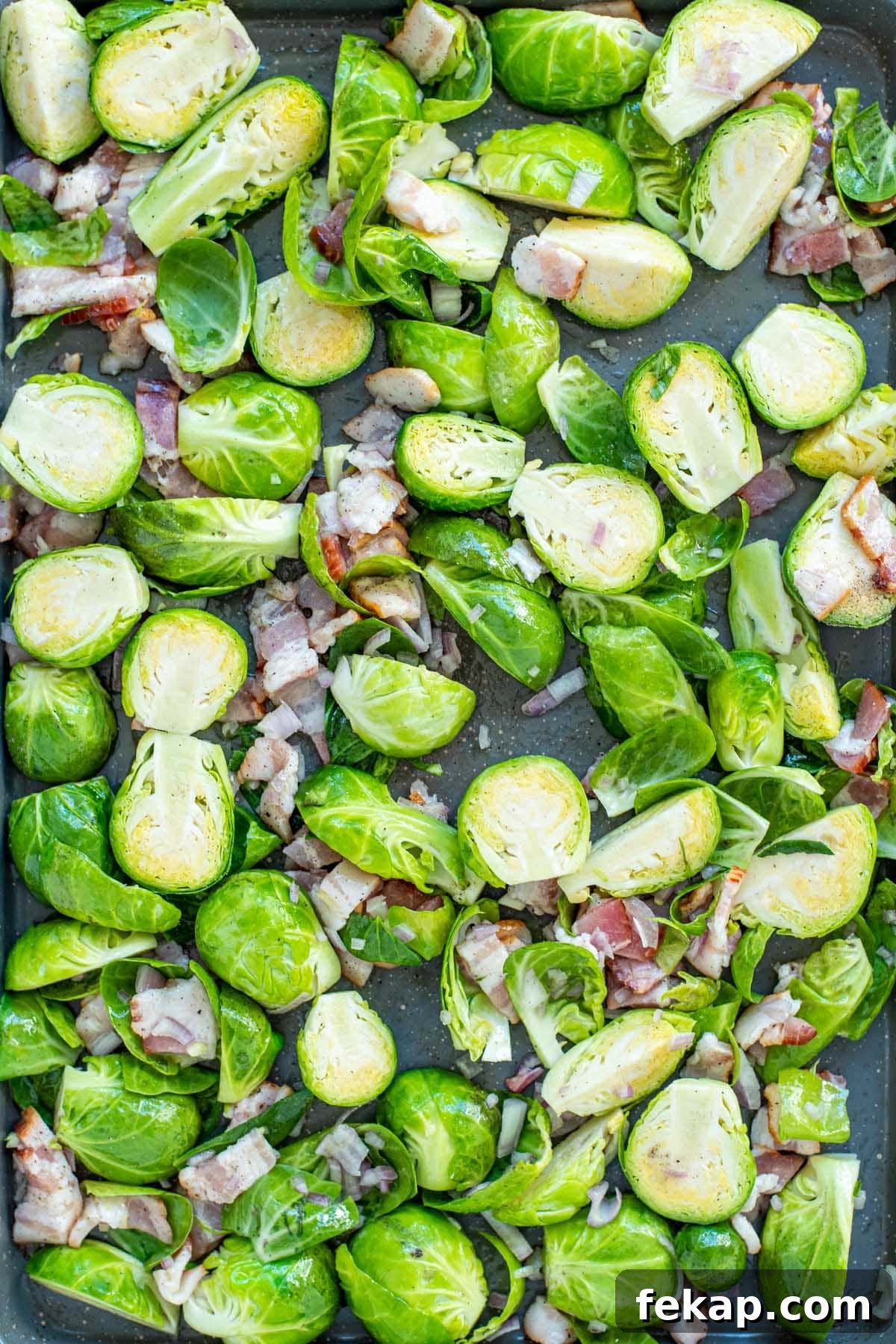 Uncooked Brussels sprouts, chopped shallots, and chopped bacon laid out on a baking sheet.