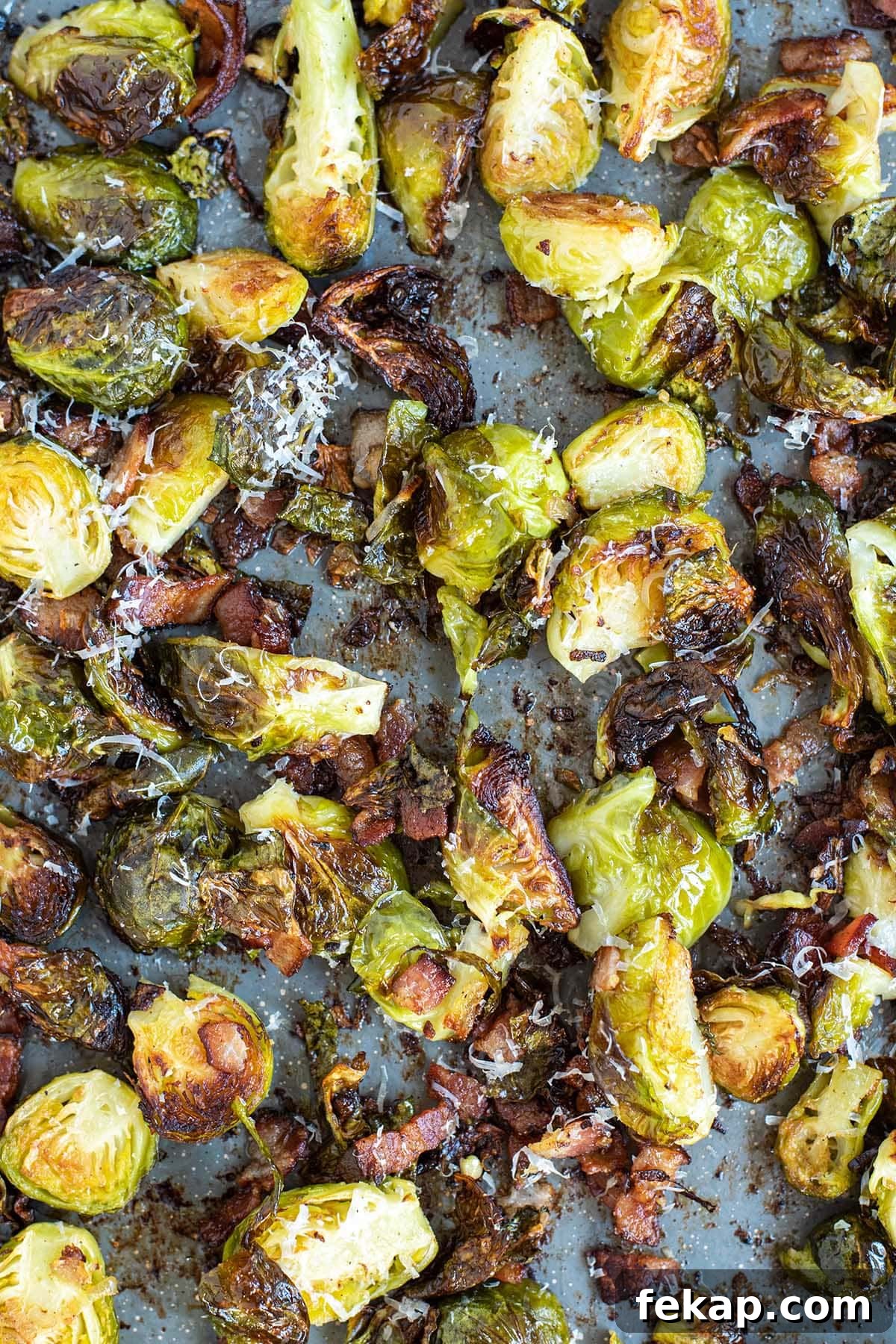 Crispy golden brussels sprouts topped with fresh grated parmesan cheese on a baking sheet.