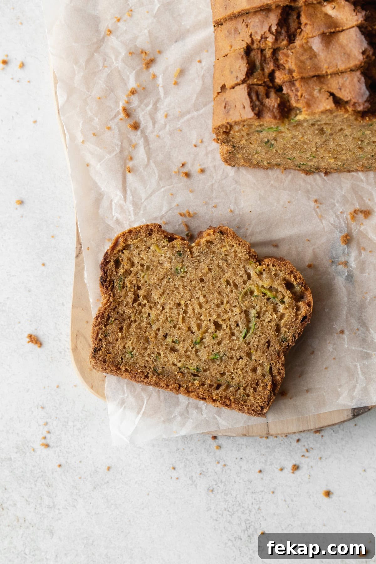 A slice of gluten free zucchini bread on a parchment-lined wooden board, with the more slices to the side.