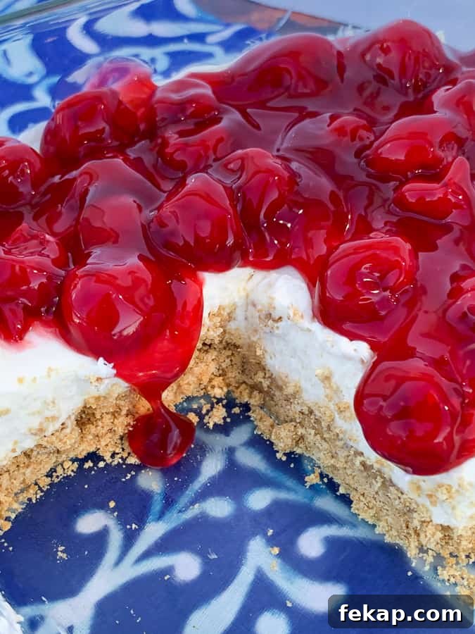 No-Bake Cherry Delight Recipe 4 Cherry pie filling poured overtop of delight dessert in 9 inch square pan on blue napkin