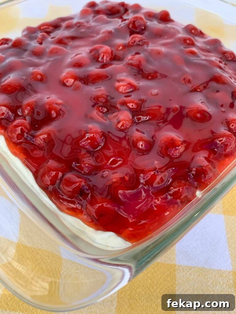 No-Bake Cherry Delight Recipe 10 Cherry pie filling poured over whipping cream and cream cheese mixture on a graham cracker crust