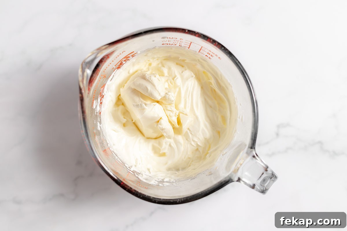 Cream cheese is added to the whipped cream and powdered sugar in the mixing bowl.
