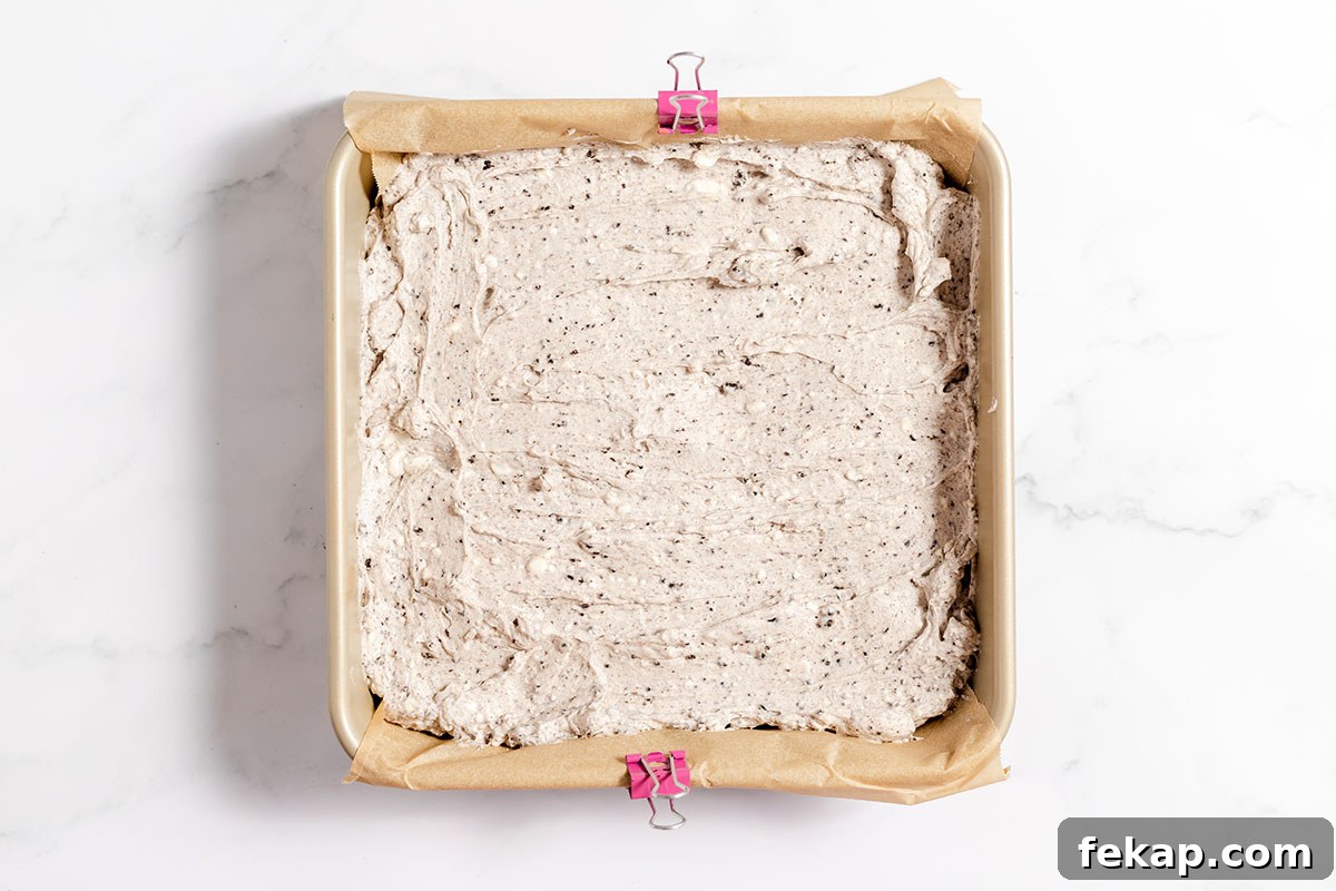 Baked Cookies and cream brownies in a parchment-lined baking pan with a creamy Oreo topping.