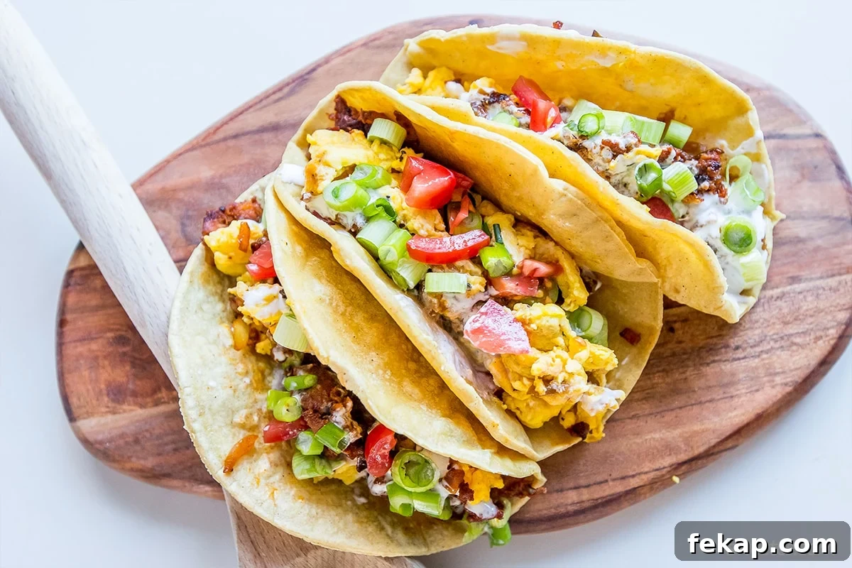 Chorizo Breakfast Tacos with Spicy Eggs 2 Three spicy breakfast tacos with scrambled eggs, tomatoes, green onions, and cheese in tortillas on a wooden board