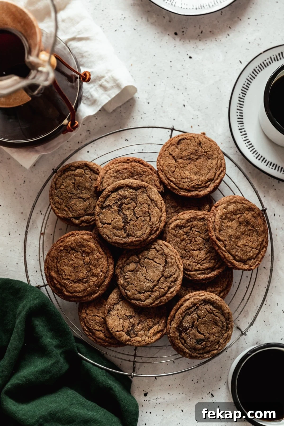 Chewy Coffee Cookies Recipe with Rich Espresso Flavor 2 A round cooling rack topped with coffee cookies on a grey speckled table next to a dark green linen, cup of coffee, and Chemex.