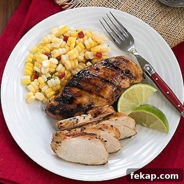 Mustard, Garlic, Lime Marinated Chicken Breasts is flavored with the BEST chicken marinade! Overhead view of marinated chicken and sides on a white dinner plate with a fork and lime wedges.