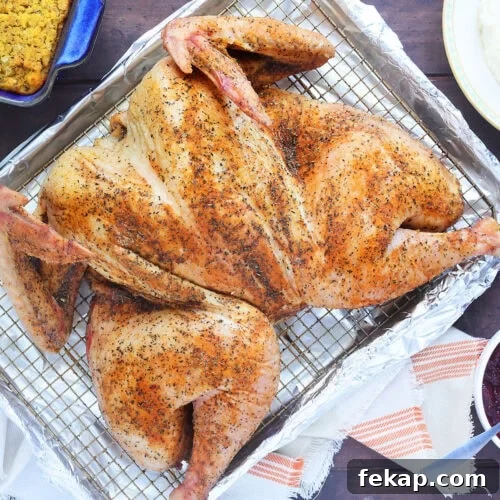 Smoked spatchcocked turkey resting on a rack on a foil lined baking sheet.