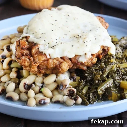 Chicken fried steak topped with country gravy on a plate with a pile of black-eyed peas and turnip greens.