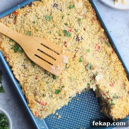 Wooden spatula laying on top of a pan of turkey tetrazzini. Two servings have been removed and are sitting on plates to the side.