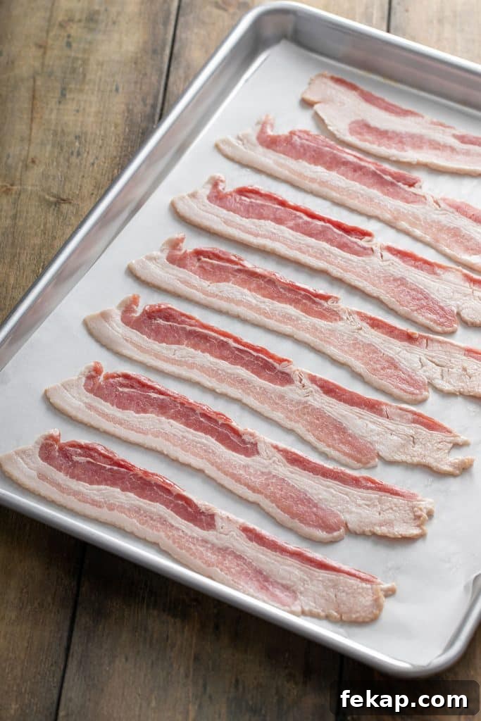 Crispy Oven-Baked Bacon: Perfectly Roasted Every Time 5 Raw bacon strips on a parchment paper lined baking sheet.