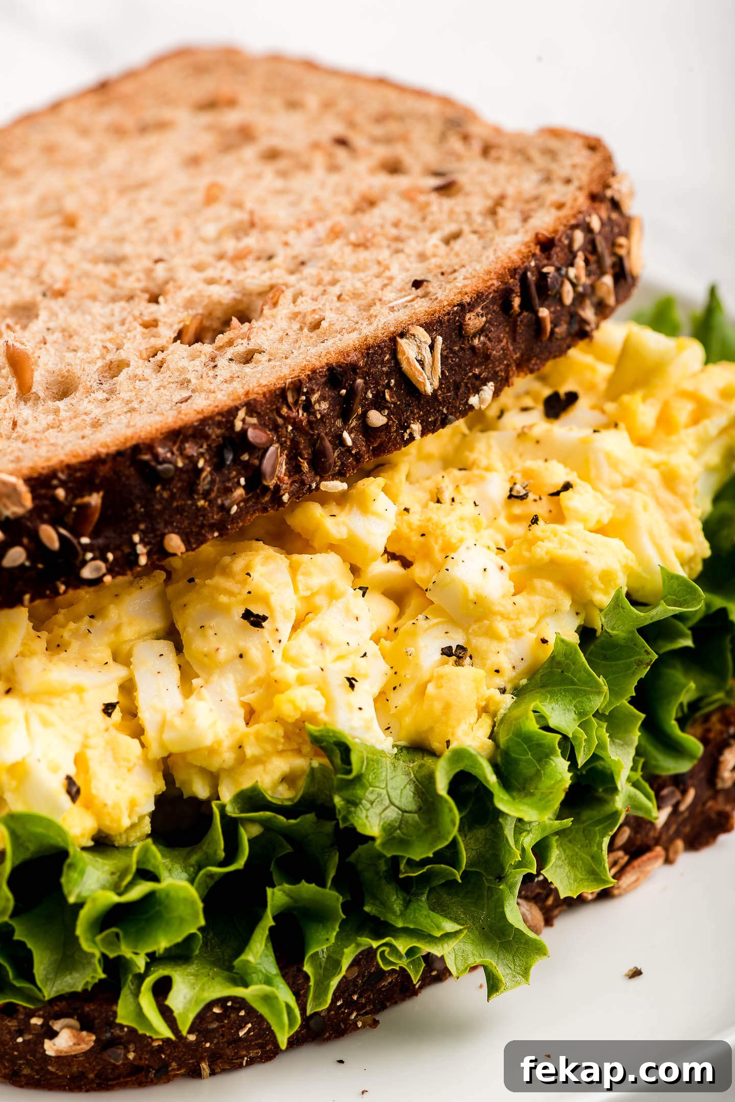 Egg salad on lettuce between two slices of whole grain bread.