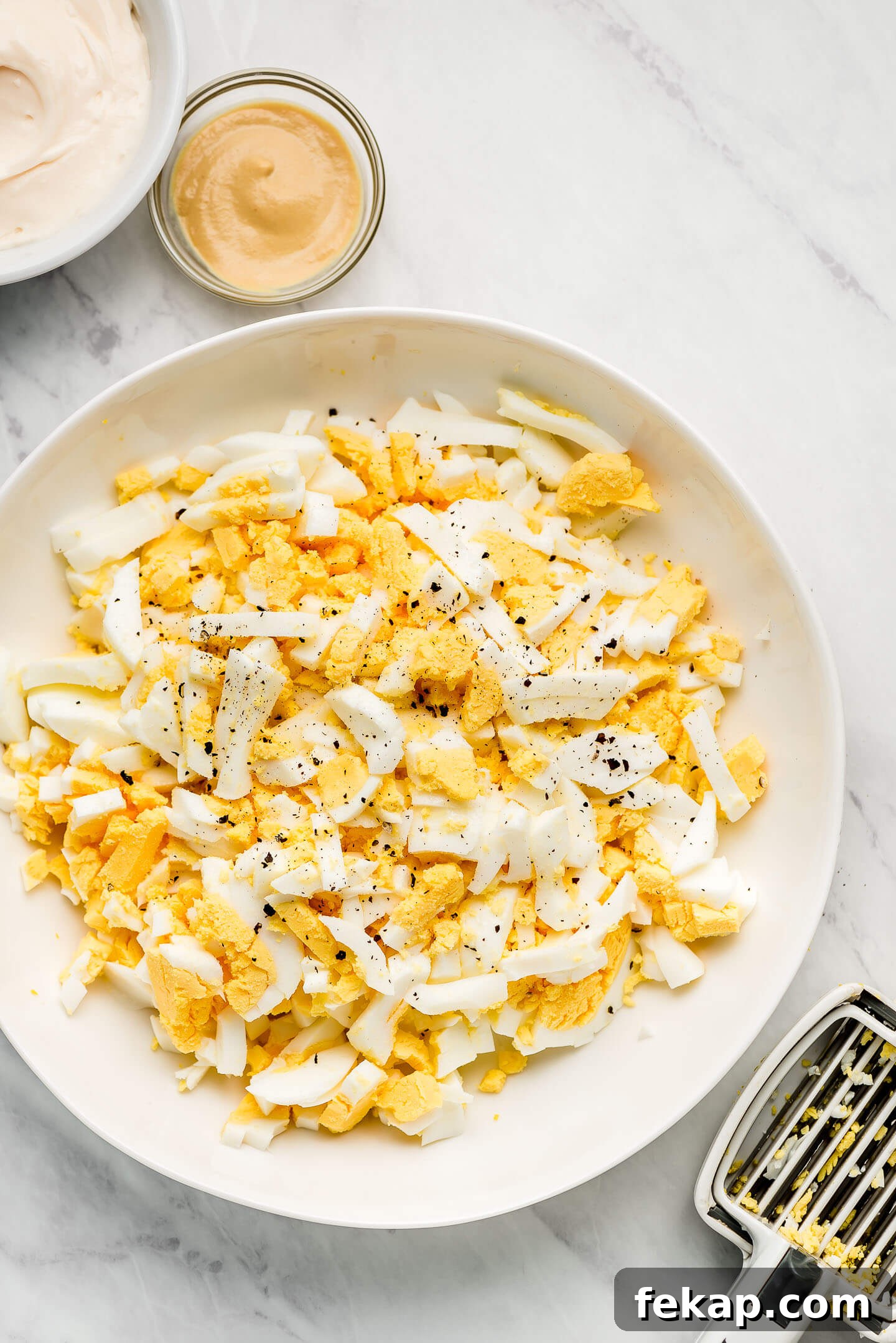 A bowl of chopped hard boiled eggs and bowls of mayo and mustard to the side.