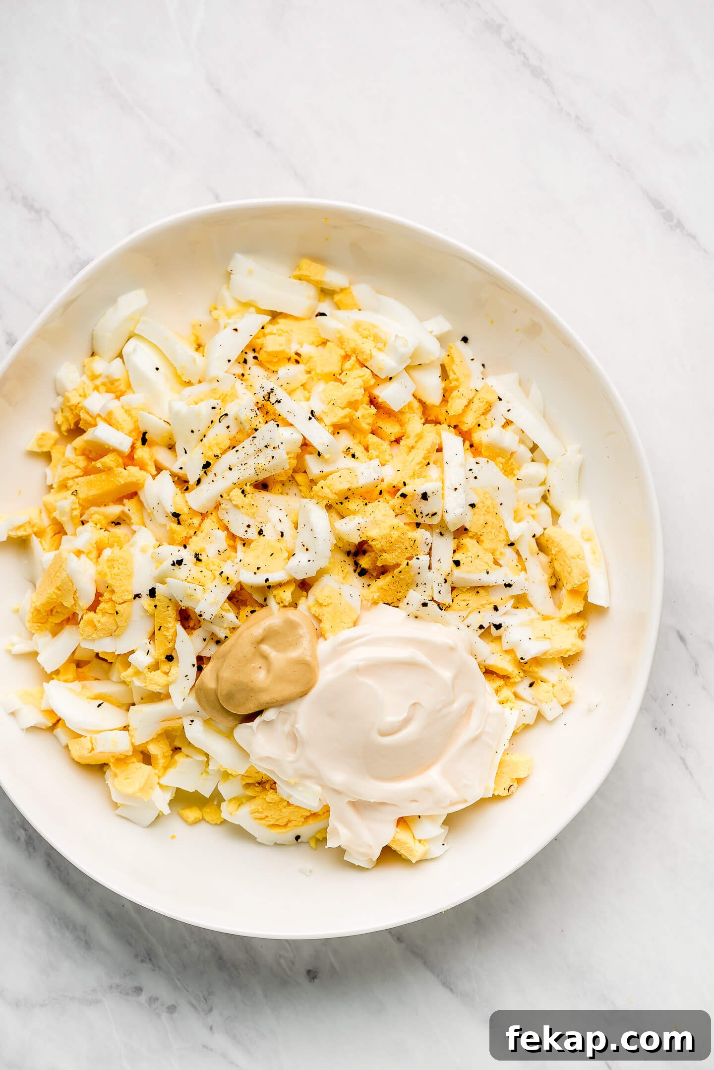 A bowl of chopped hard boiled eggs, mayonnaise, mustard, and salt & pepper.