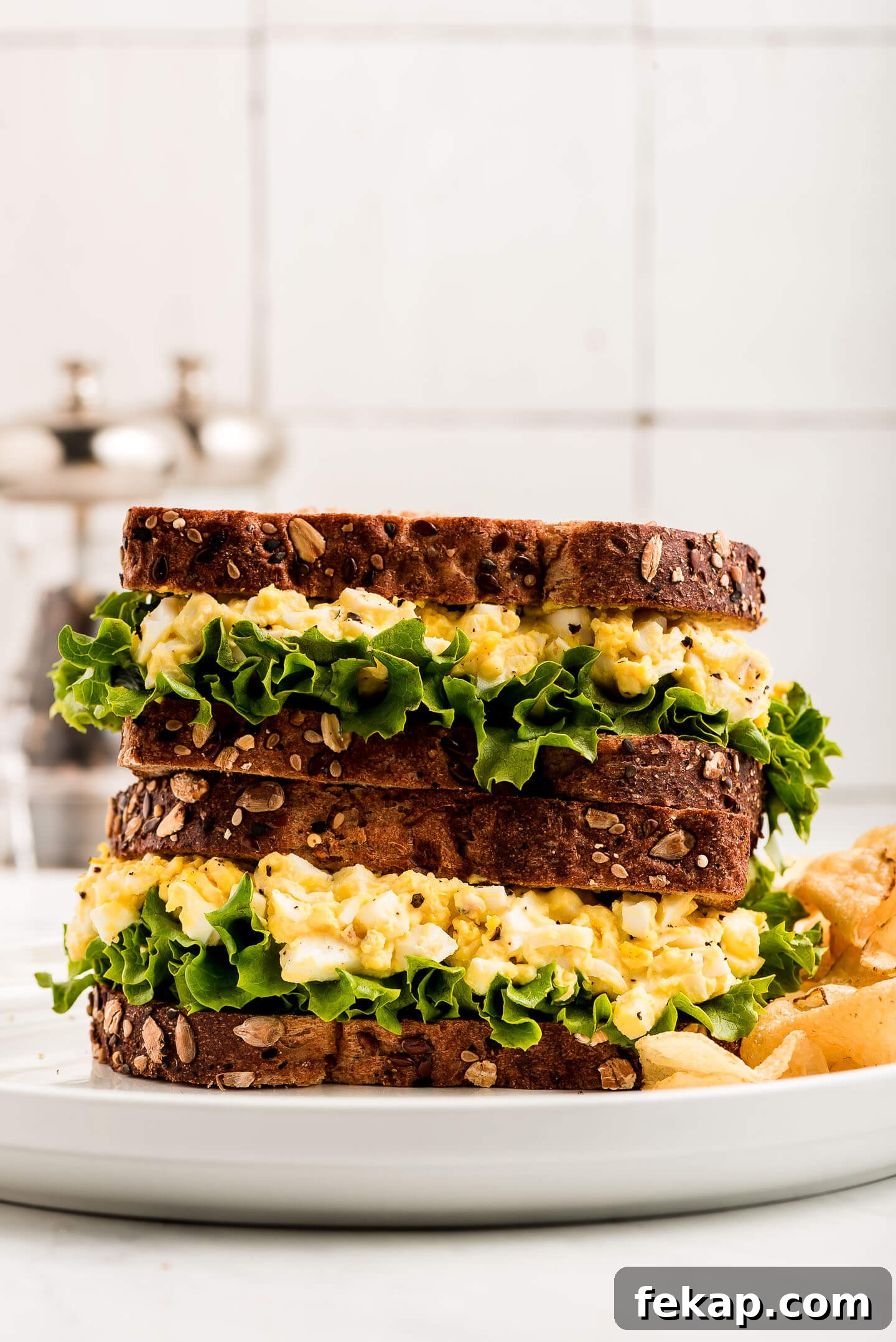 Two Egg Salad Sandwiches stacked on top of each other on a plate.