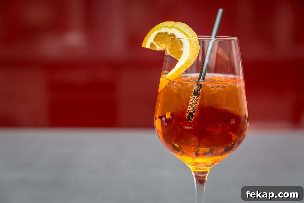 Raspberry wine spritzer in a wine glass with orange slice and straw.