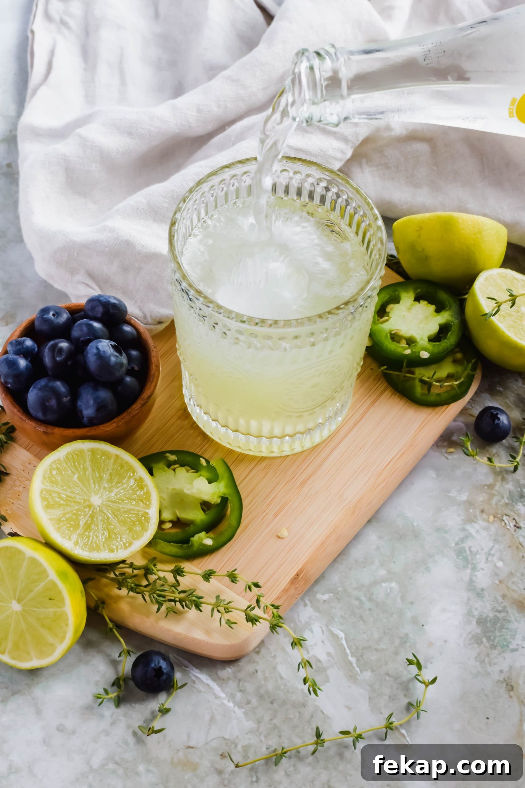 Blueberry Texas Ranch Water Cocktail Recipe 4 Topo Chico being poured into cocktail glass with lime juice and tequila on wood plank.